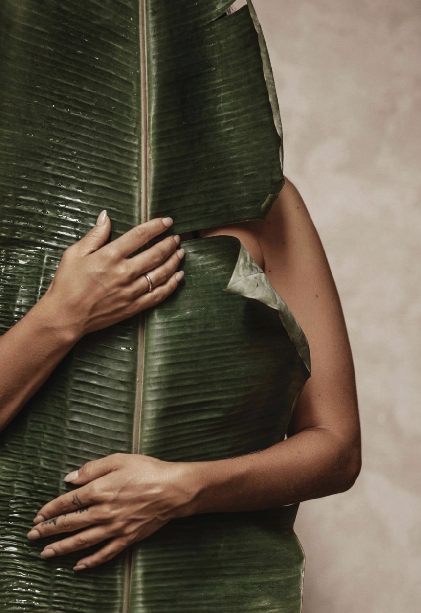 Woman wrapped in a banana leaf against a clay plaster wall